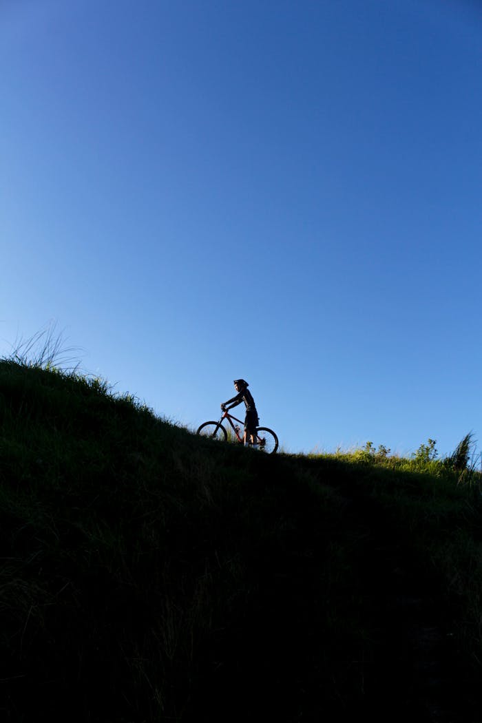 Silhouette of a cyclist ascending a grassy hill against a clear blue sky in Calabarzon.